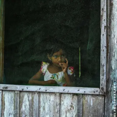 Menina ribeirinha à janela de casa de madeira